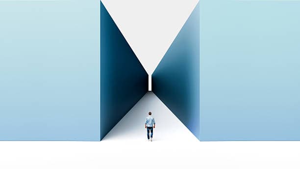A person walking toward a narrow gap between two tall walls