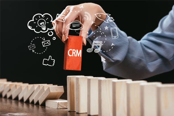 Hand lifting a red CRM block out of a row of falling dominoes