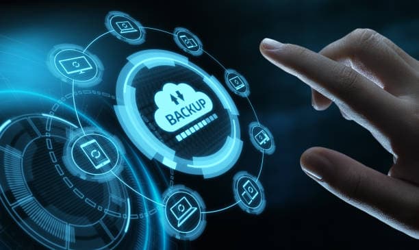 Hand touching a glowing cloud backup icon surrounded by connected device icons